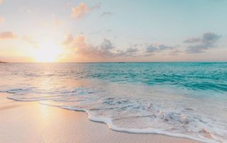Sun setting over clear blue ocean with beach-Things to remember during uncertain times.