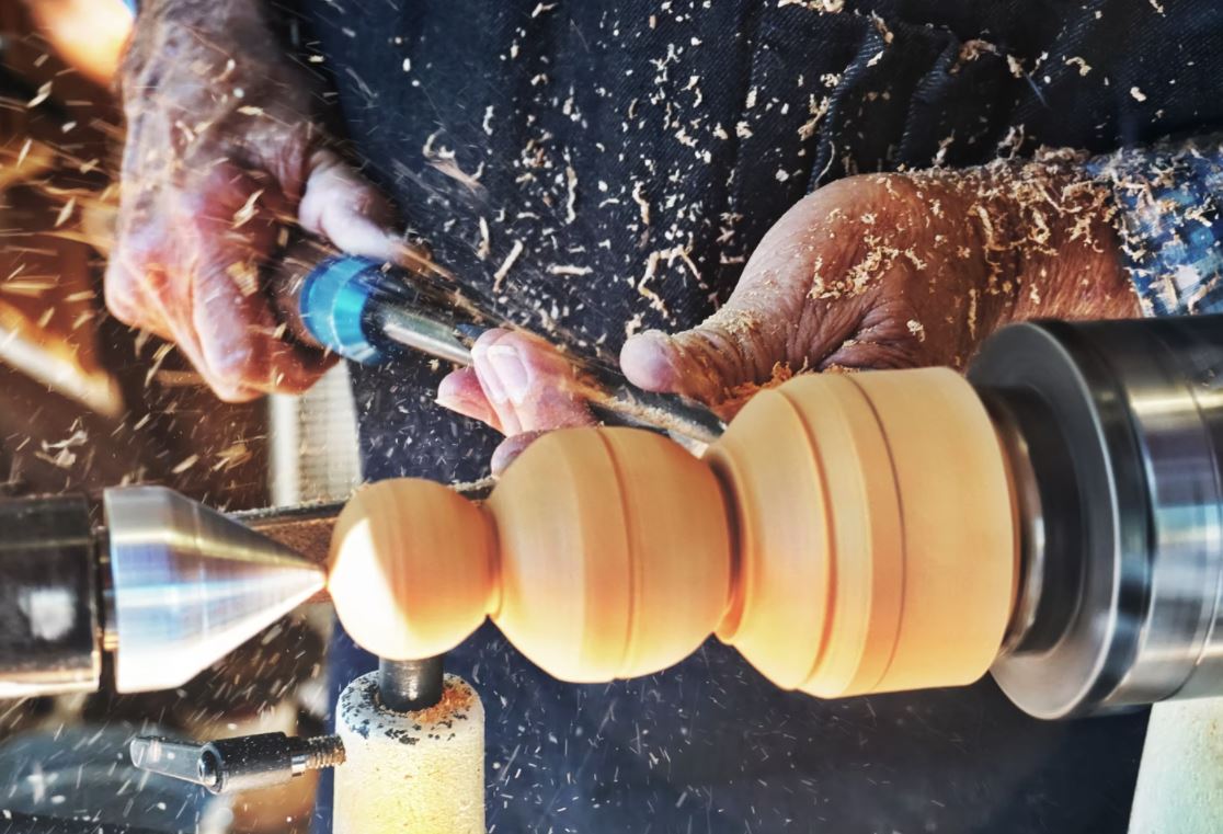 Hands crafting the leg of a stool.