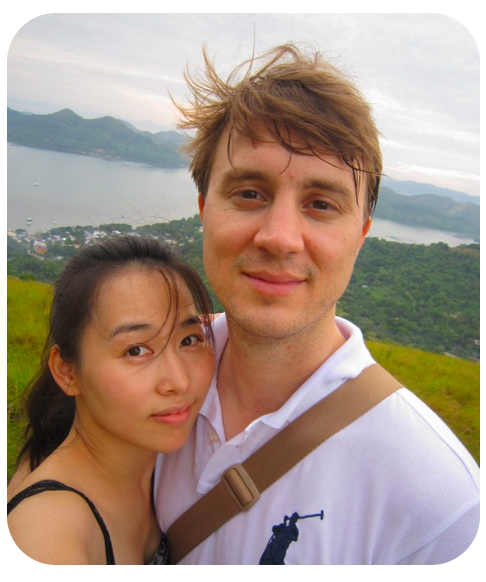 Matt Moser and an adult female stand on a hill in front of a body of water and mountains.