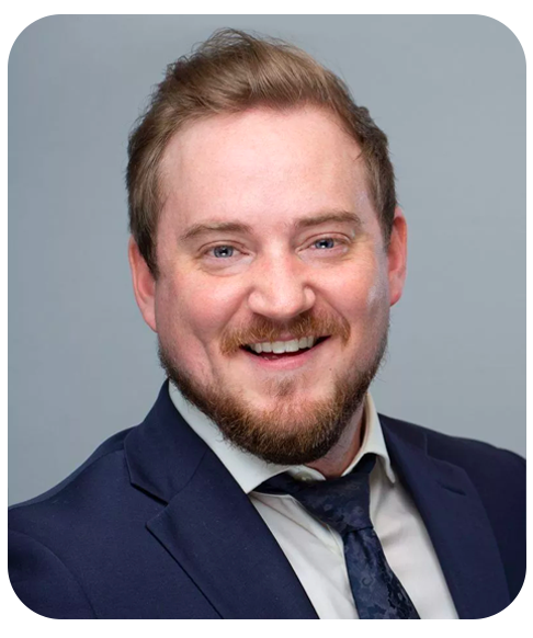 A head shot of Conrad Beauchamp. He is smiling and wearing a suit and tie.