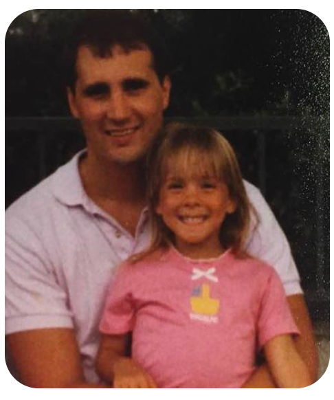 An older photograph of Craig Moser holding a young girl on his lap. Both are smiling.