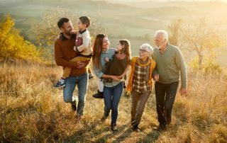 A happy multi-generational family of grandparents, adult children, and grandchildren, walks up a sunny hill.
