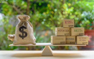 A balanced scale holds a burlap sack with a dollar sign on the left and several boxes on the right, which read ETFs, Stocks, REITs, Commodities, Bonds, and Mutual Funds.