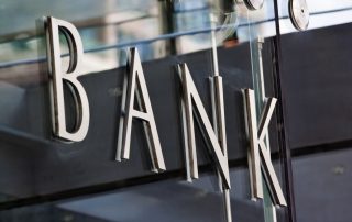 Modern exterior glass doors with the word "BANK" mounted on them in silver letters.
