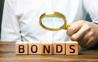A person holds a magnifying glass over four blocks that spell BONDS.